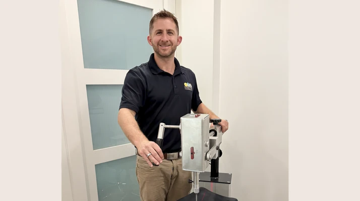Person standing beside a chiropractic instrument in a bright clinical treatment room.